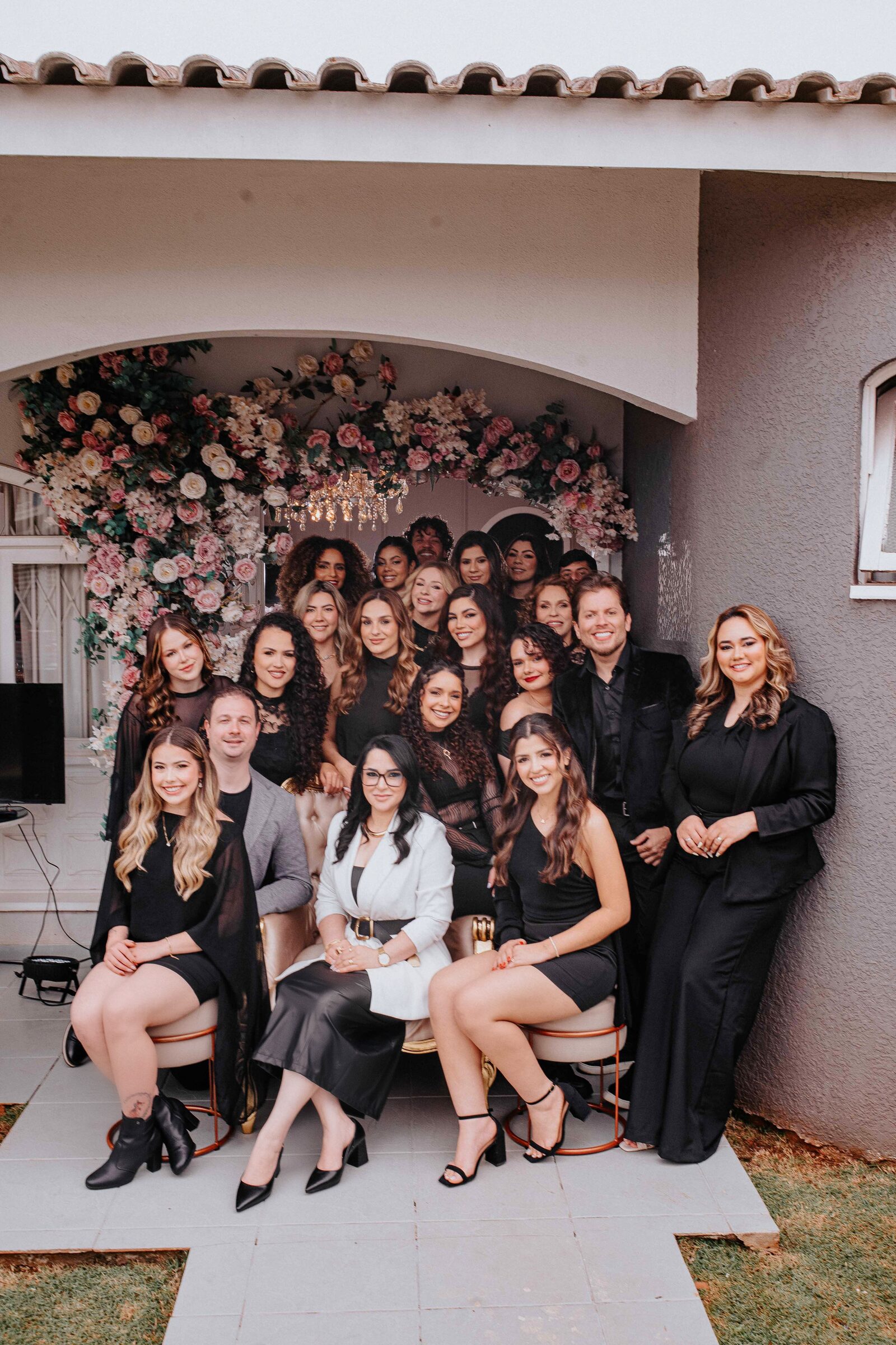 Equipe completa do Studio Gisele Raffaelli posando sob o arco floral da entrada do espaço