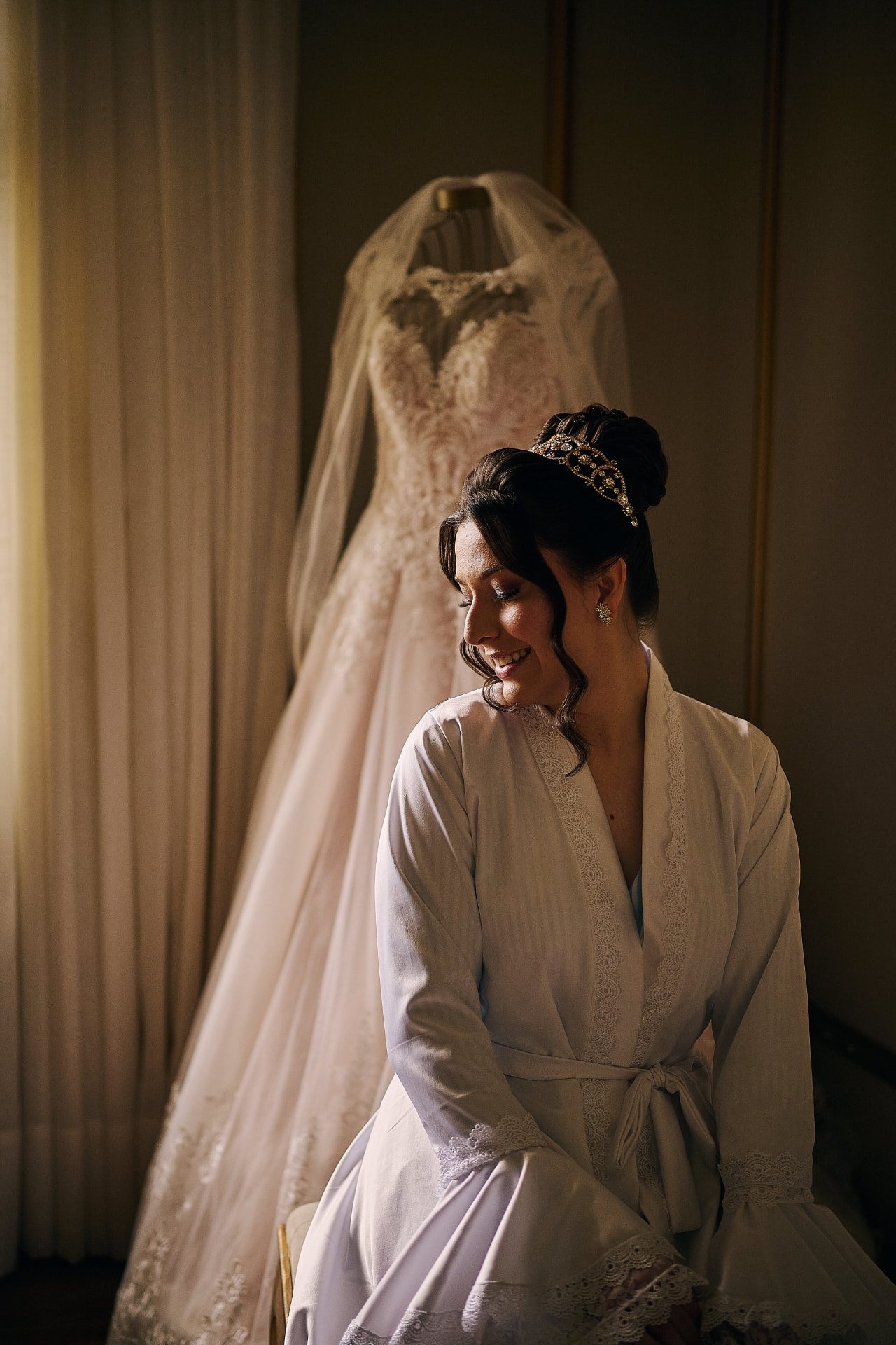 Noiva de robe sorrindo ao lado do vestido de noiva em manequim dourado